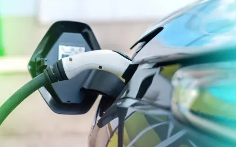 Ładowanie samochodu elektrycznego. Wtyczka podłączona do portu ładowania, zielony kabel biegnie do stacji.