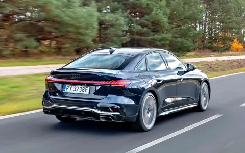 Ciemny Audi A4 B10 pędzi po drodze, otoczony jesiennym lasem.