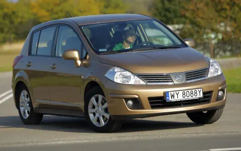 Złoty Nissan Tiida z mężczyzną za kierownicą jedzie po drodze.