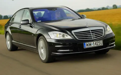 Czarny Mercedes-Benz W221 pędzi po drodze, mijając pola.
