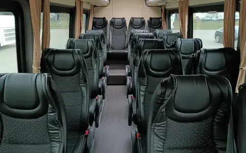 Wnętrze busa z rzędami czarnych, wygodnych siedzeń. Widać, ile miejsc ma bus osobowy, gotowy na podróż.