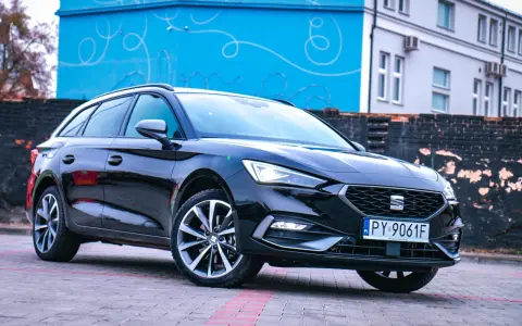 Czarny Seat Leon Sportstourer z polskimi tablicami rejestracyjnymi stoi na brukowanym placu przed budynkiem z niebieską, ozdobną ścianą.