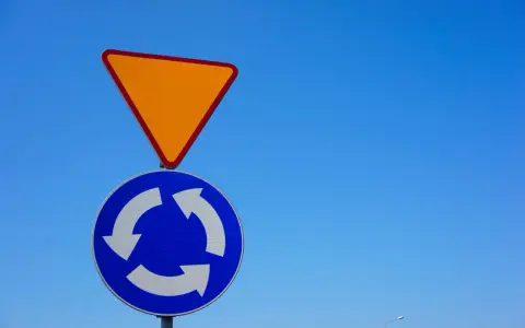 Znak ustąp pierwszeństwa i znak informujący o ruchu okrężnym na tle błękitnego nieba.