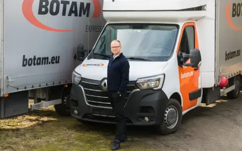Mężczyzna stoi przed białym busem do transportu międzynarodowego marki BOTAM.
