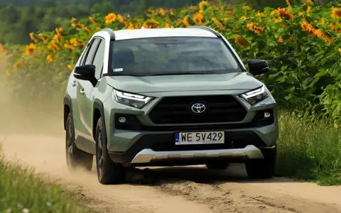 Zielona Toyota RAV4 jedzie po piaszczystej drodze, otoczona słonecznikami. To jeden z najmniej awaryjnych aut, gotowy na każdą przygodę.