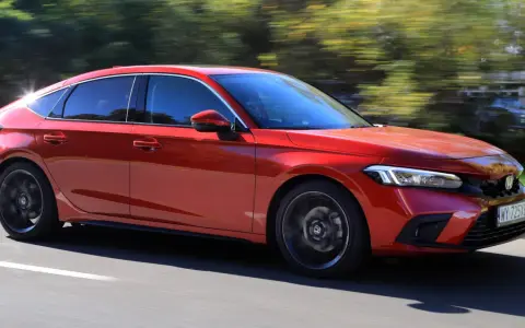 Czerwony Honda Civic 11. generacji pędzi po drodze, otoczony zielenią drzew.