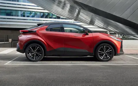 Czerwona Toyota C-HR Hybrid na tle nowoczesnego budynku. Zastanawiasz się, ile kosztuje Toyota C-HR Hybrid?