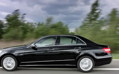 Czarny Mercedes E350 pędzi po drodze, mijając rozmyte zielone drzewa.