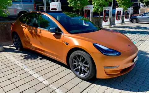 Pomarańczowa Tesla Model 3 na ładowarce. Zastanawiasz się, ile przejedzie Tesla na jednym ładowaniu?
