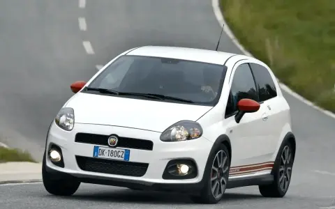Biały Fiat Punto Evo Abarth z czerwonymi lusterkami pędzi po zakręcie drogi.