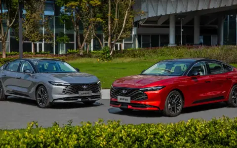 Dwa nowe Fordy Mondeo mk6, jeden czerwony, drugi szary, stoją obok siebie na tle nowoczesnego budynku i zieleni.