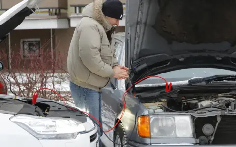 Mężczyzna podłącza kable rozruchowe do samochodu, by odpalić toyotę hybrydę na kable.
