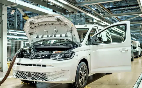 Biały samochód elektryczny na linii produkcyjnej. Widać otwartą maskę i drzwi, a także elementy silnika. Powstają tu polskie samochody.