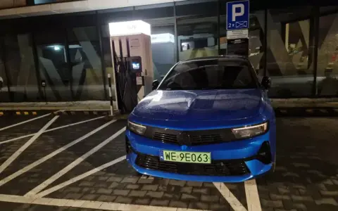 Niebieski samochód elektryczny pod ładowarką. Zastanawiasz się, ile się płaci za ładowanie samochodu elektrycznego?