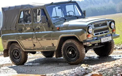 Zielony UAZ z plandeką, marka samochodu na u, pokonuje błotnisty teren.