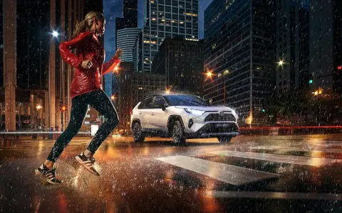 Biegaczka w deszczowy wieczór w mieście, obok niej biała Toyota RAV4 Hybrid. Zastanawiasz się, ile pali Toyota RAV4 Hybrid?