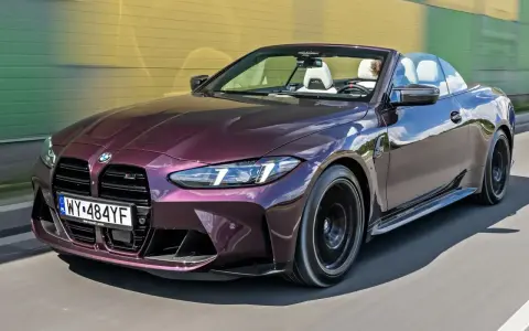 Fioletowe BMW M4 Competition kabriolet pędzi po drodze, odsłaniając białe wnętrze i sportowe detale.