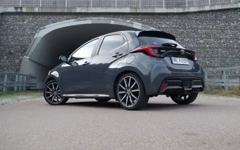 Szary Toyota Yaris GR Sport z czarnym spojlerem i dyfuzorem, zaparkowany przed tunelem.