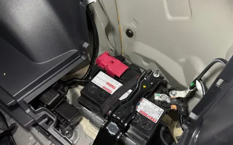 Akumulator 12V w Toyocie Prius znajduje się w bagażniku, pod plastikową osłoną. Widoczne są dwa akumulatory, jeden z czerwonym zabezpieczeniem.