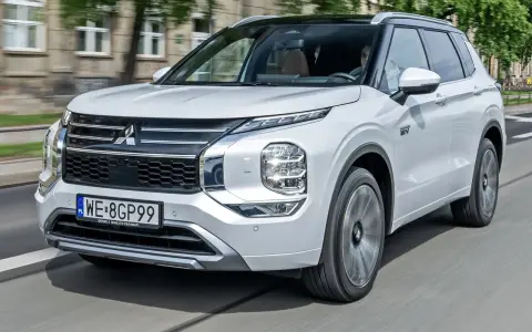 Biały Mitsubishi Outlander PHEV, jeden z nowoczesnych modeli tej marki, jedzie po mieście.