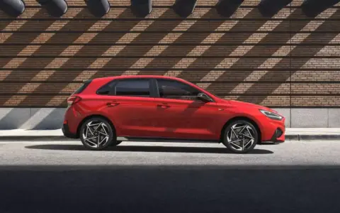 Czerwony Hyundai i30 stoi na tle ceglanej ściany z ciekawymi cieniami.