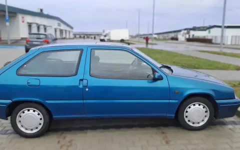 Niebieski Citroen ZX stoi na parkingu. W tle widać budynki i białą ciężarówkę.