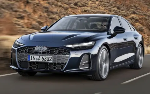 Elegancki, ciemnogranatowy Audi A6 sunie po drodze, z kierowcą w okularach za kierownicą.