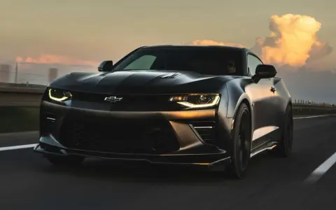 Czarny Chevrolet Camaro pędzi po autostradzie o zachodzie słońca.