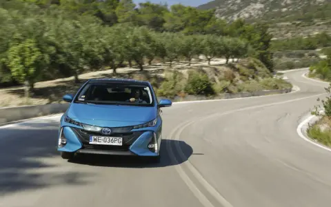 Niebieska Toyota Prius pokonuje zakręt na malowniczej drodze. Zastanawiasz się, ile pali Toyota Prius? Ten model jest znany z oszczędności.
