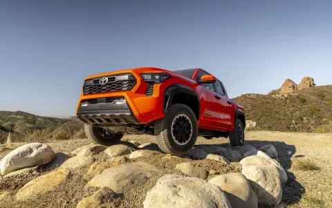Pomarańczowy Toyota pickup pokonuje kamienisty teren na tle wzgórz.