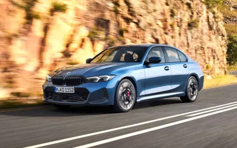 Niebieskie BMW klasy średniej jedzie po krętej drodze w skalistym krajobrazie.