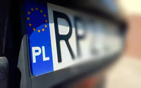 Zbliżenie na polską tablicę rejestracyjną z symbolem UE. Litery "PL" i fragment innych znaków sugerują, że pojazd jest w trakcie wyrejestrowania.