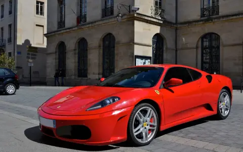 Czerwone Ferrari F430 na brukowanej ulicy przed kamienicą. Zastanawiasz się, ile kosztuje najtańsze Ferrari?