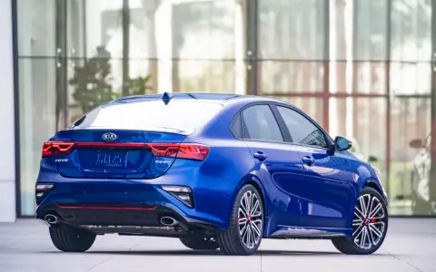 Niebieskie Kia Forte GT z czerwonymi akcentami, zaparkowane przed nowoczesnym budynkiem.