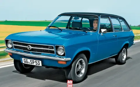 Niebieski Opel Ascona w wersji kombi jedzie po drodze, za nim pola i niebo.