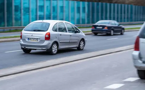 Srebrny Citroën Xsara Picasso jedzie po drodze, mijając inne samochody.