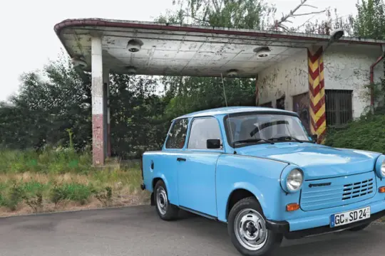 Niebieski trabant stoi przed opuszczoną stacją benzynową.