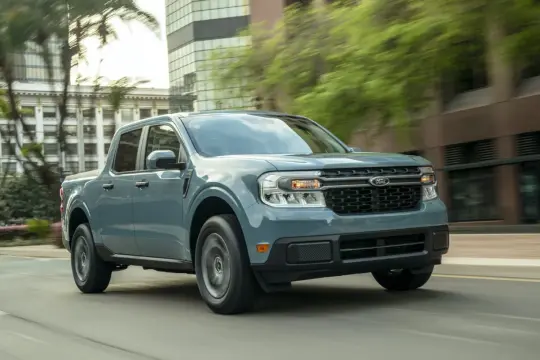 Maverick, niebieski pickup Forda, jedzie ulicą miasta, otoczony zielenią i budynkami.