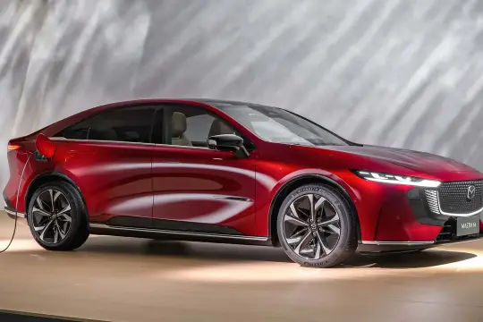 Elegancka, czerwona Mazda 6e, podłączona do ładowania, prezentuje nowoczesny design i ekologiczne podejście do motoryzacji.