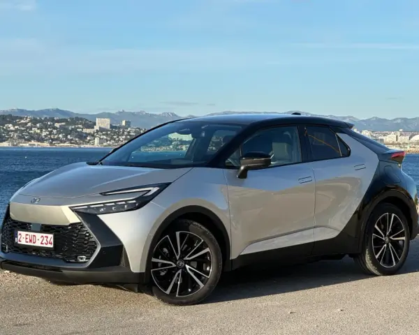 Srebrno-czarna Toyota C-HR na tle morza i miasta. Zastanawiasz się, ile przejedzie hybryda Toyoty na jednym ładowaniu?