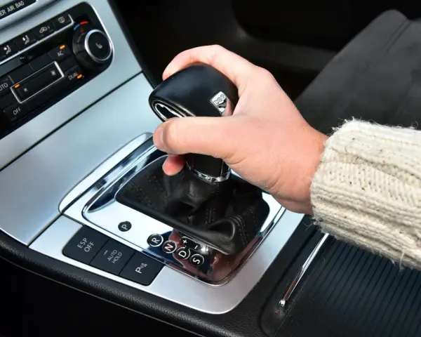 Dłoń trzyma gałkę zmiany biegów w samochodzie. Widoczna jest automatyczna skrzynia biegów DSG z przyciskami ESP, Auto Hold i czujnikami parkowania.