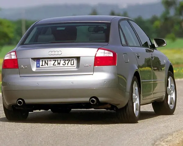 Srebrne Audi B6 sedan z tablicą rejestracyjną IN ZW 370 jedzie po asfaltowej drodze wśród zieleni i żółtych kwiatów.