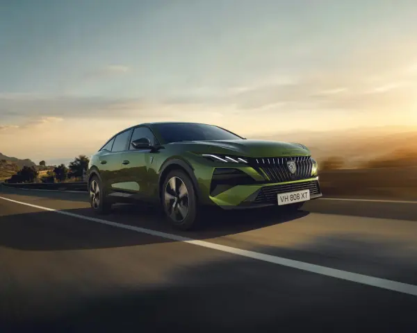 Zielony Peugeot 408 GT sunie po krętej drodze, otoczony malowniczym krajobrazem o zachodzie słońca.