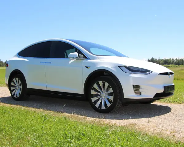 Biała Tesla Model X na tle łąki i lasu. Zastanawiasz się, ile kosztuje najtańsza Tesla?
