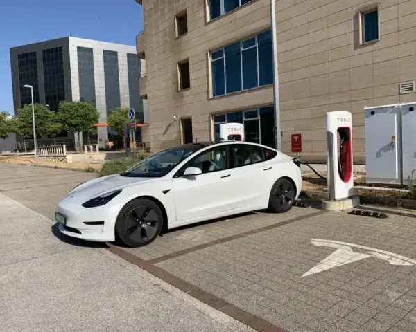 Biały Tesla Model 3, zasilany energią, czeka na ładowanie. Zastanawiasz się, ile koni ma ten model?