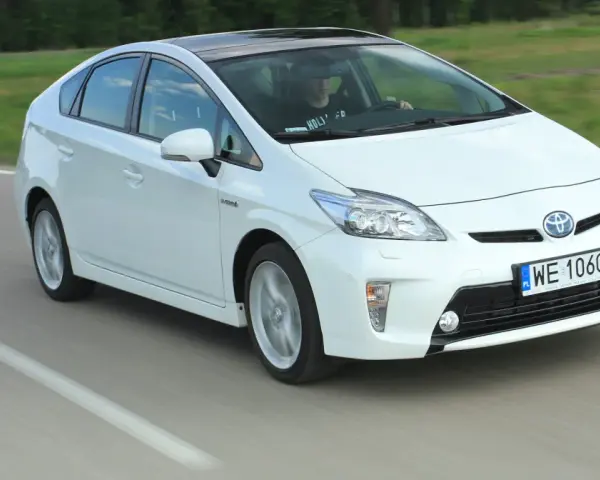 Biała Toyota Prius w ruchu. Czy warto kupić ten hybrydowy samochód?