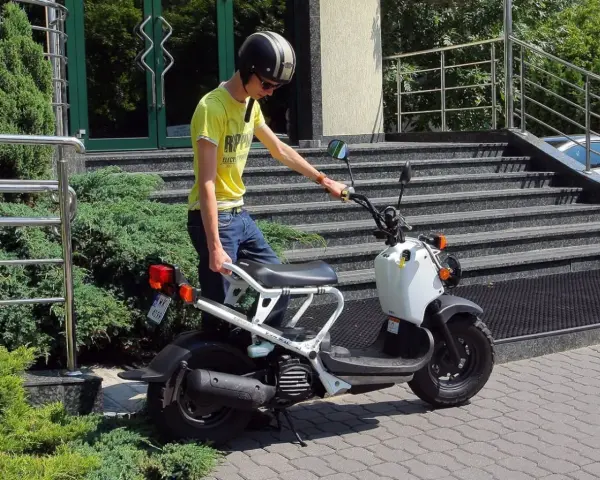 Chłopak w kasku i żółtej koszulce przy białym skuterze. Zastanawiasz się, ile kosztuje karta motorowerowa?