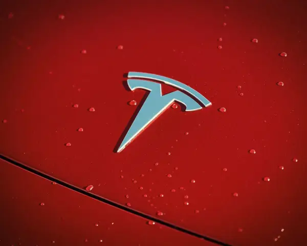 Błyszczące logo Tesli na czerwonej karoserii z kroplami deszczu. Czy Tesla jest tylko elektryczna?