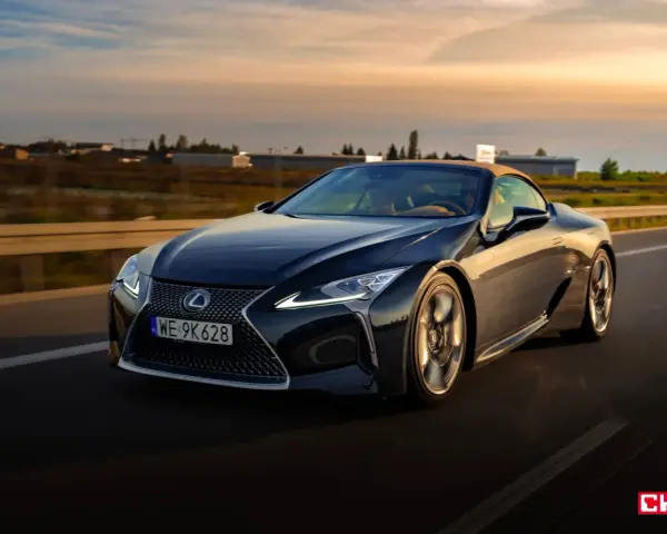 Ciemny Lexus LC 500 z beżowym dachem sunie po drodze podczas zachodu słońca. Sprawdź jego lexus lc 500 cena.