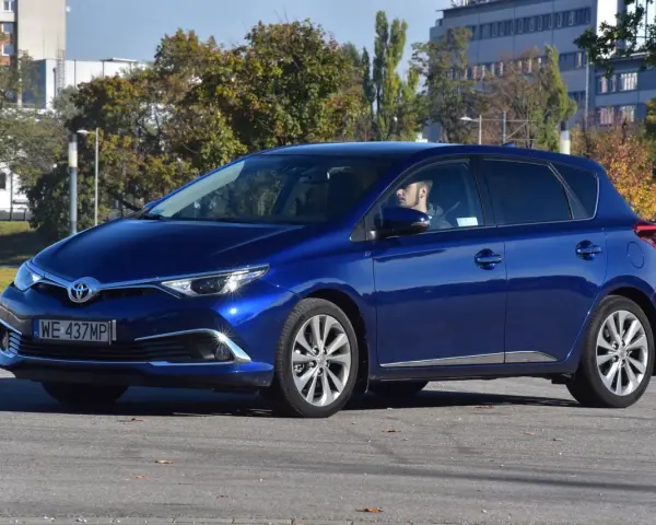 Niebieska Toyota Auris Hybrid, z kierowcą za kierownicą, na parkingu. Zastanawiasz się, ile pali Toyota Auris Hybrid?